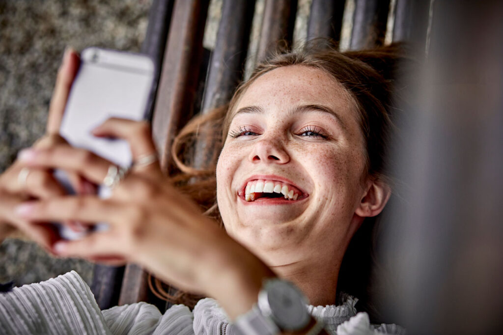 Junge Frau mit Smartphone freut sich über den schnellen Online-Abschluss einer Zahnzusatzversicherung mit Sofortschutz.